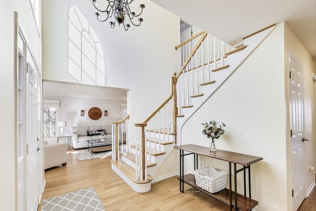 foyer with stairs, an inviting chandelier, a high ceiling, and wood finished floors