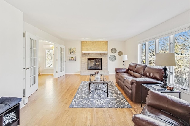 living area with a wealth of natural light, a large fireplace, french doors, and light wood-style flooring