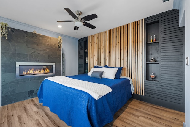 bedroom featuring a tile fireplace, ceiling fan, ornamental molding, wood finished floors, and recessed lighting