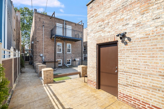 back of property featuring a balcony, a patio area, fence, and brick siding