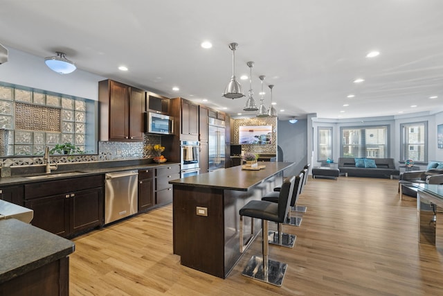 kitchen with dark countertops, appliances with stainless steel finishes, a kitchen breakfast bar, and a sink