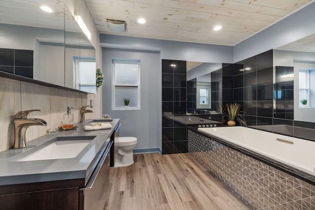 bathroom featuring a garden tub, wood finished floors, a sink, and toilet