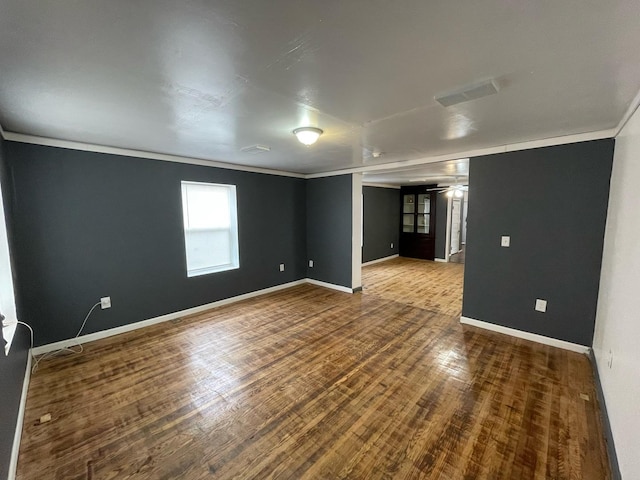 empty room with ornamental molding, visible vents, baseboards, and wood finished floors