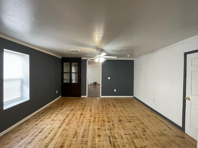 unfurnished room with wood finished floors, visible vents, a ceiling fan, baseboards, and crown molding