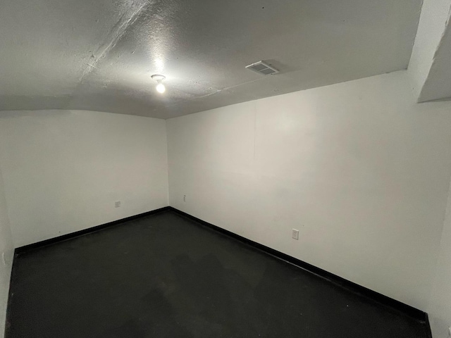 spare room with a textured ceiling, concrete floors, visible vents, and baseboards