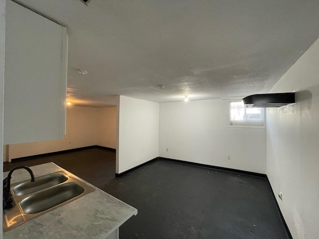 below grade area with a sink, a textured ceiling, and baseboards