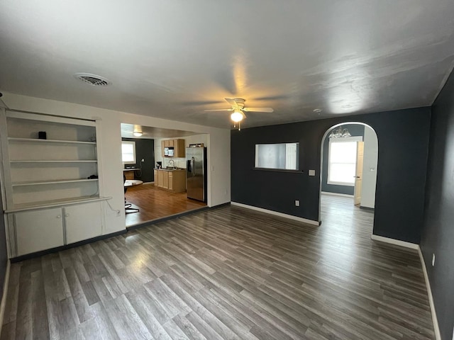 unfurnished living room with arched walkways, dark wood-type flooring, visible vents, and baseboards