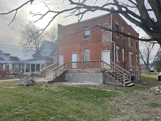 back of house featuring a sunroom, brick siding, and a lawn