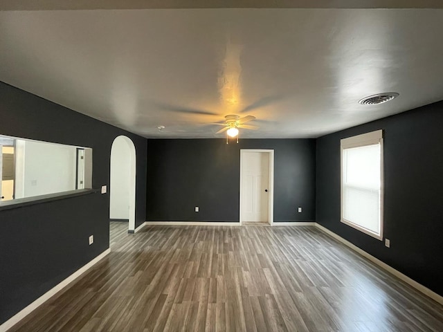 empty room with baseboards, visible vents, a ceiling fan, arched walkways, and wood finished floors