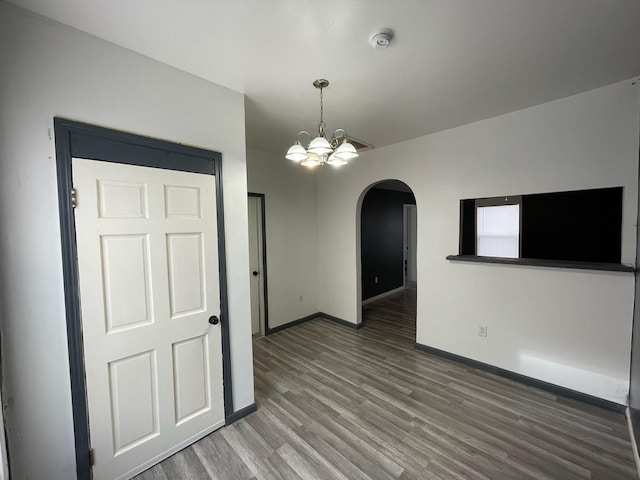 unfurnished room featuring arched walkways, a notable chandelier, baseboards, and wood finished floors