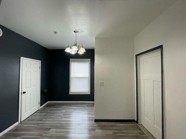 unfurnished dining area with baseboards, a chandelier, and wood finished floors