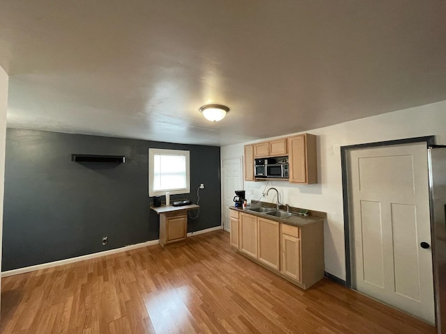 kitchen featuring light wood finished floors, baseboards, stainless steel microwave, light brown cabinets, and a sink