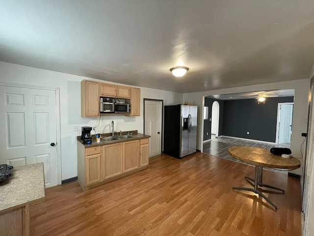 kitchen featuring arched walkways, light wood finished floors, appliances with stainless steel finishes, light brown cabinets, and a sink