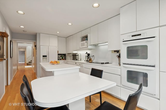 kitchen with recessed lighting, white appliances, white cabinetry, light countertops, and a center island