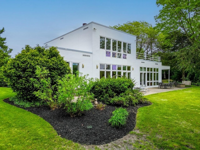 rear view of property with a yard, a patio area, a balcony, and stucco siding