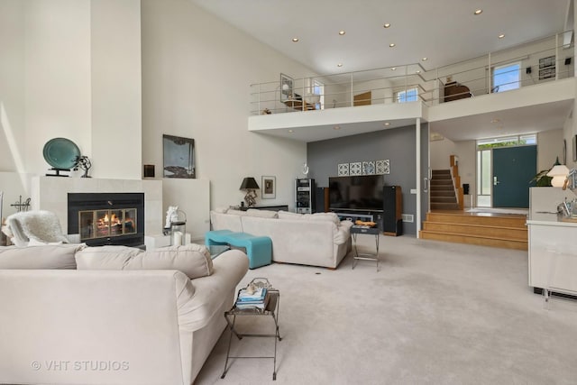 living room with a tiled fireplace, a towering ceiling, stairway, carpet flooring, and recessed lighting