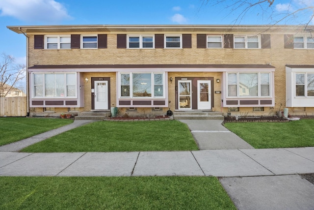 view of property with brick siding, a front yard, and fence