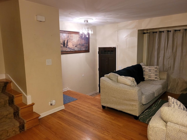 living room featuring an inviting chandelier, stairs, baseboards, and wood finished floors