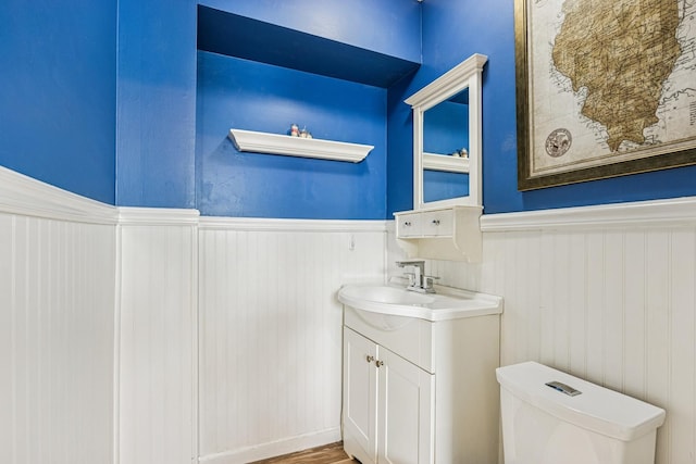 bathroom with a wainscoted wall, toilet, wood finished floors, and vanity