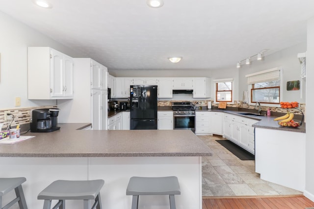 kitchen with a peninsula, gas range, black refrigerator with ice dispenser, and a sink