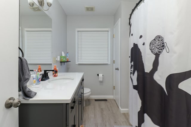 full bath with visible vents, toilet, vanity, wood finished floors, and baseboards