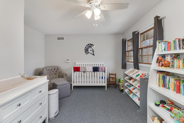 bedroom featuring a crib, ceiling fan, visible vents, and dark colored carpet