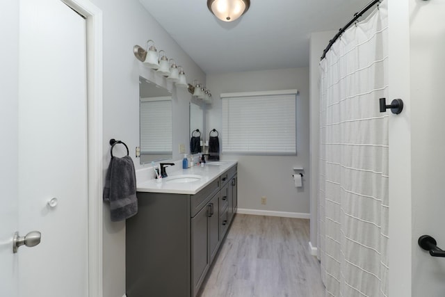 bathroom with double vanity, a sink, baseboards, and wood finished floors