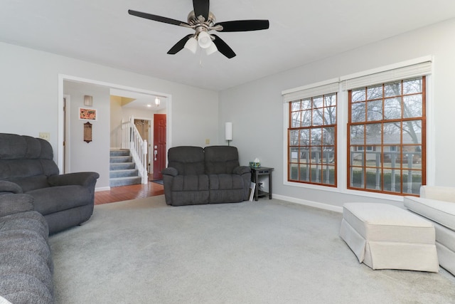 living area with light carpet, baseboards, stairway, and ceiling fan