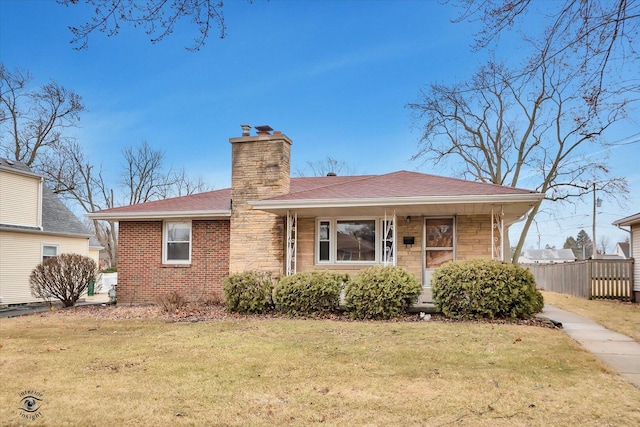 view of front of house featuring brick siding, roof with shingles, a chimney, a front yard, and fence