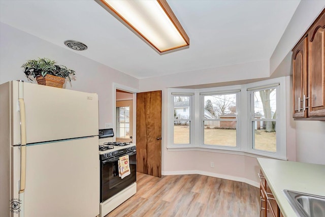 kitchen with range with gas stovetop, light wood finished floors, light countertops, visible vents, and freestanding refrigerator