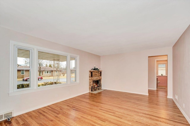 unfurnished living room featuring light wood-type flooring, a brick fireplace, visible vents, and baseboards