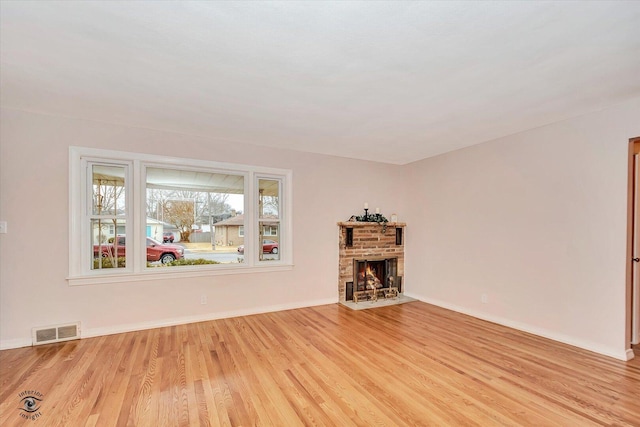 unfurnished living room with baseboards, visible vents, a fireplace, and light wood finished floors