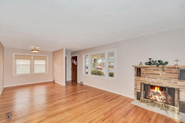 living area with a brick fireplace, plenty of natural light, visible vents, and wood finished floors