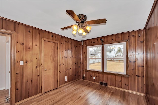 spare room featuring wooden walls, light wood-type flooring, visible vents, and a ceiling fan