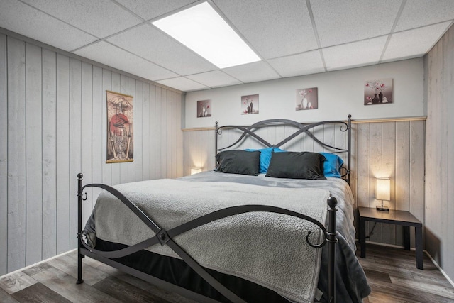 bedroom featuring wood walls, wood finished floors, and a paneled ceiling