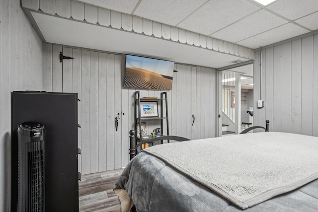 bedroom with wood walls, wood finished floors, and a paneled ceiling