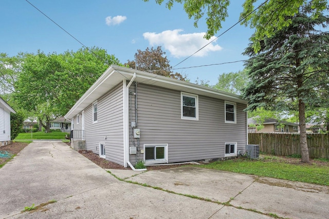 view of side of home featuring fence, central AC, and concrete driveway