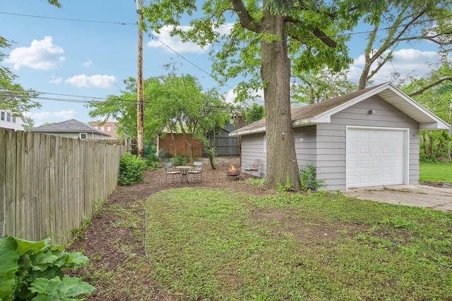 view of yard with an outdoor structure, driveway, a detached garage, and fence