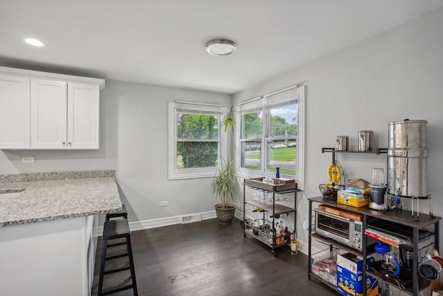 kitchen featuring light stone counters, dark wood-style flooring, visible vents, white cabinets, and baseboards