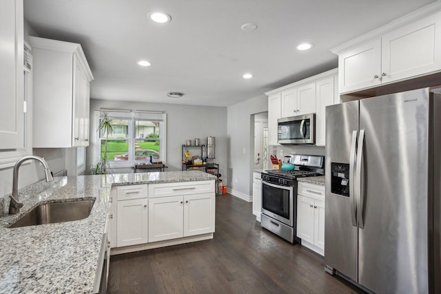 kitchen featuring white cabinets, appliances with stainless steel finishes, dark wood-type flooring, a peninsula, and a sink