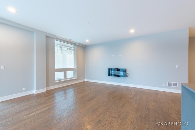 unfurnished living room featuring a glass covered fireplace, visible vents, baseboards, and wood finished floors