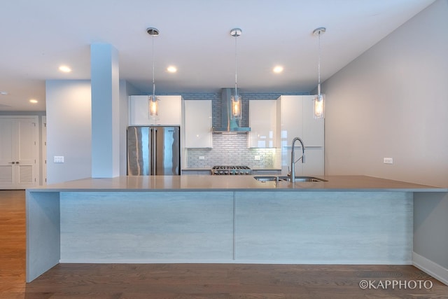 kitchen with dark wood-type flooring, high end refrigerator, a sink, wall chimney exhaust hood, and pendant lighting