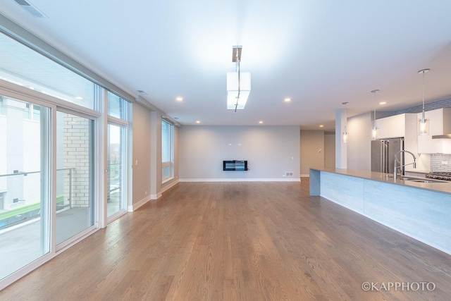 unfurnished living room with wood finished floors, a sink, visible vents, and baseboards