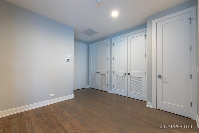 unfurnished bedroom with visible vents, baseboards, dark wood finished floors, and two closets