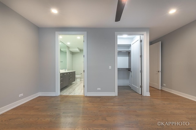 unfurnished bedroom with ensuite bathroom, a spacious closet, baseboards, and wood finished floors