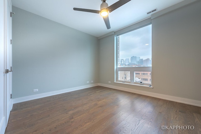 spare room with dark wood-style flooring, a city view, visible vents, and baseboards