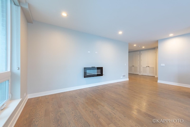 unfurnished living room with light wood-type flooring, recessed lighting, baseboards, and a glass covered fireplace