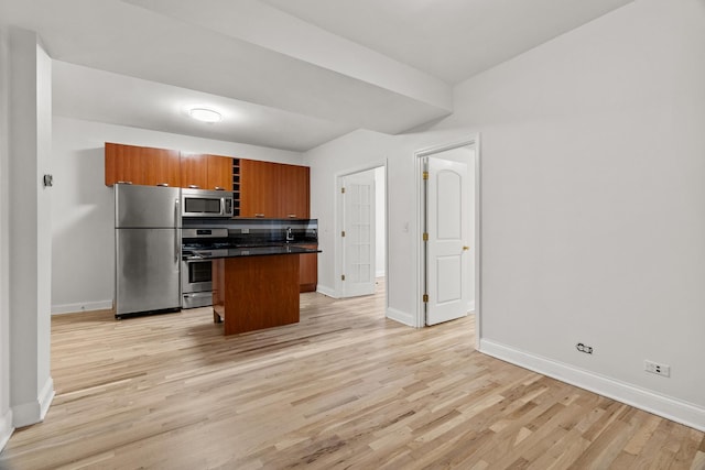 kitchen with stainless steel appliances, light wood finished floors, brown cabinetry, and dark countertops