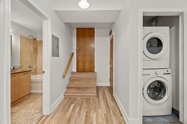 washroom with baseboards, laundry area, electric panel, and stacked washer / drying machine