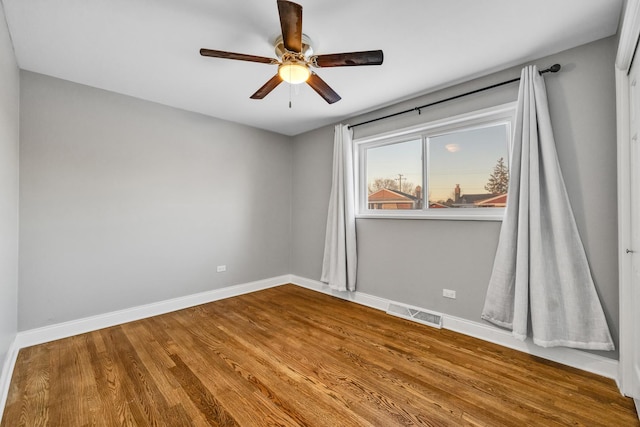 empty room featuring a ceiling fan, baseboards, visible vents, and wood finished floors